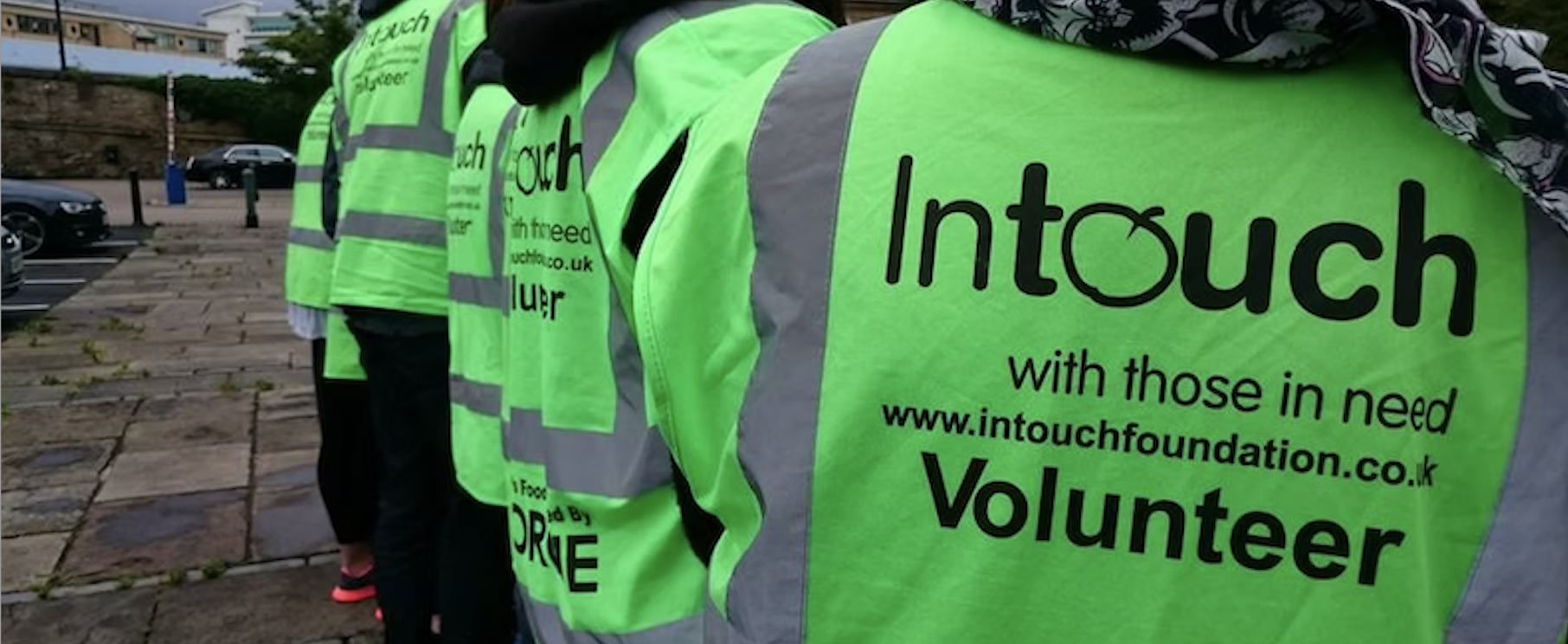 A line of people wearing green high-vis jackets that have the Intouch charity branding on the back